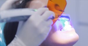 Dentist using dental curing UV lamp on teeth of patient