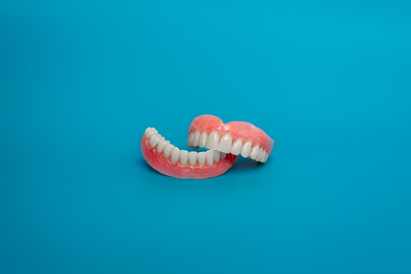 Full removable plastic denture of the jaws. Set of dentures on a blue background. Two acrylic dentures. Upper and lower jaws with fake teeth. Dentures or false teeth, close-up. Copy space