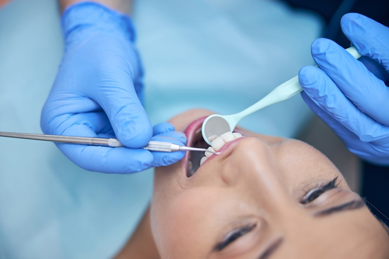 Top view close up of cheerful beautiful female lying in dental chair and being examined by professional with tools