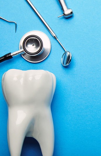 flat lay with tooth model, stethoscope and sterile dental instruments arranged on blue backdrop