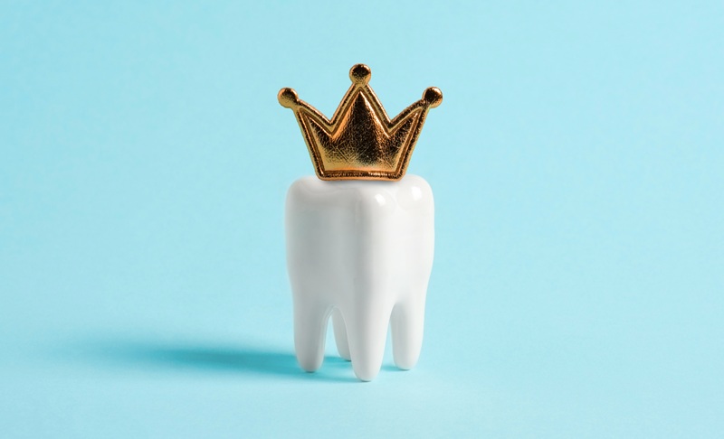 A model of a tooth with a gold crown on a light blue background