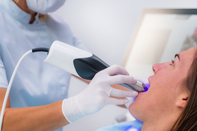 A dentist using a oral scanner, modern technology, during an appointment with a young woman.